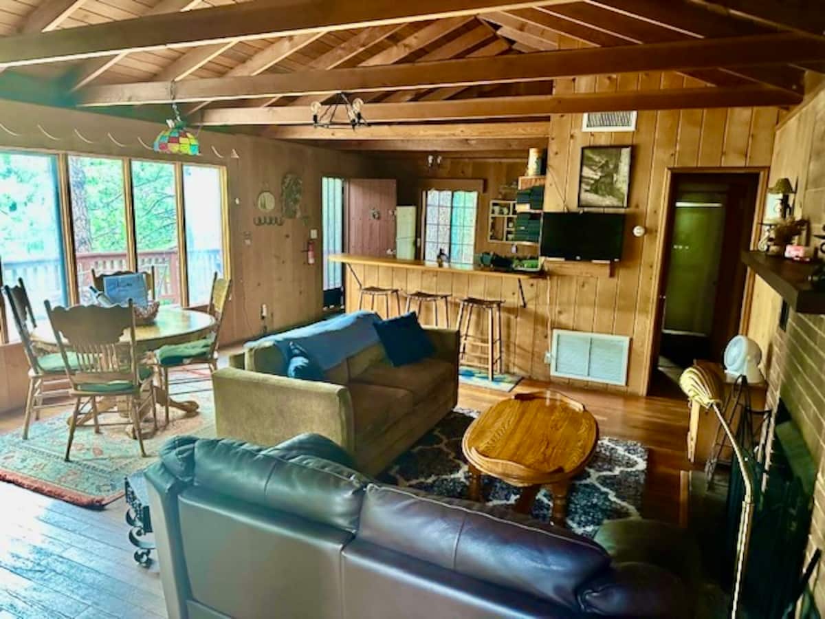Wood-paneled great room with sofas, dining area, and open kitchen